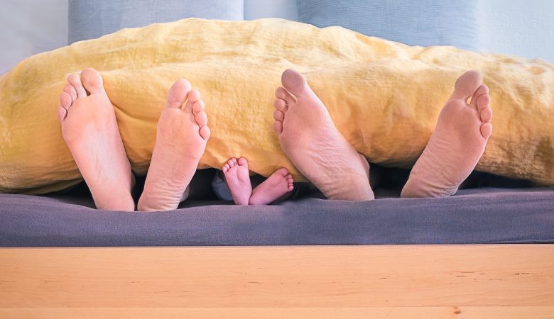 Sechs Füße gucken unter Bettdecke hervor Familie